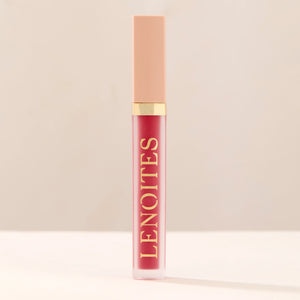 Tinted Lip Oil in Bold by Lenoites, featuring a sleek tube with a pink cap and clear body, showcasing the rich berry-red tint, displayed against a soft beige background.