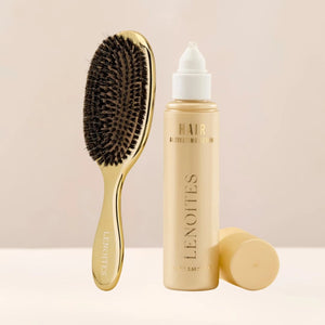 The Hair Growth Duo by Lenoites featuring a gold hairbrush and the Hair Growth Serum in a transparent bottle with a golden tone, styled against a soft light beige background.