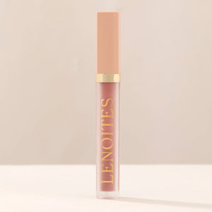 Tinted Lip Oil in Sophisticated by Lenoites, featuring a sleek tube with a pink cap and clear body, showcasing the blush tint, displayed against a soft beige background.