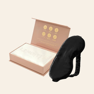 Pillowcase and Sleep Mask in Mulberry Silk by Lenoites featuring a black silk sleep mask and a white mulberry silk pillowcase presented in an open blush pink box against a soft light background.